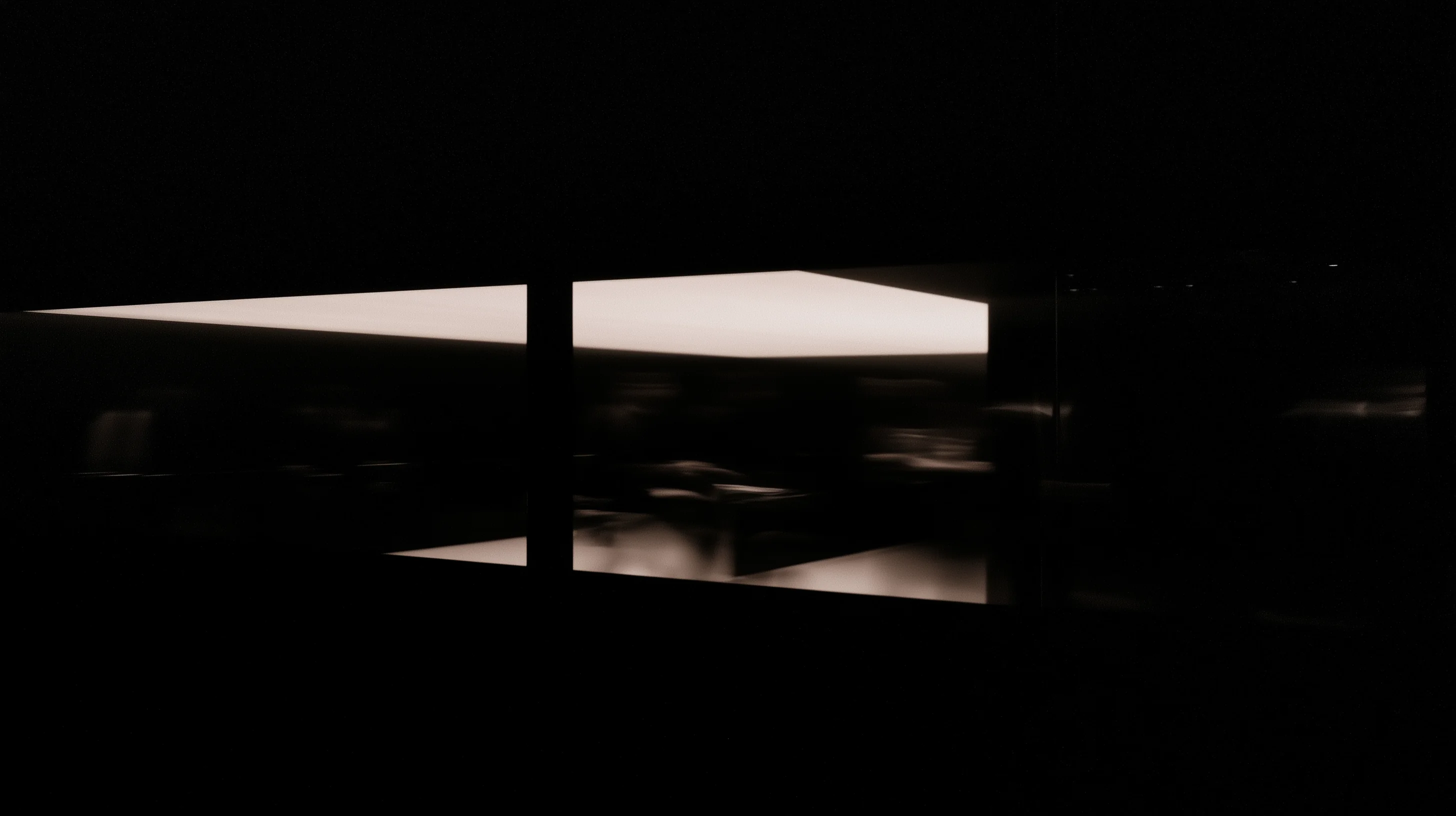 A dark architectural threshold illuminated by geometric light at night.