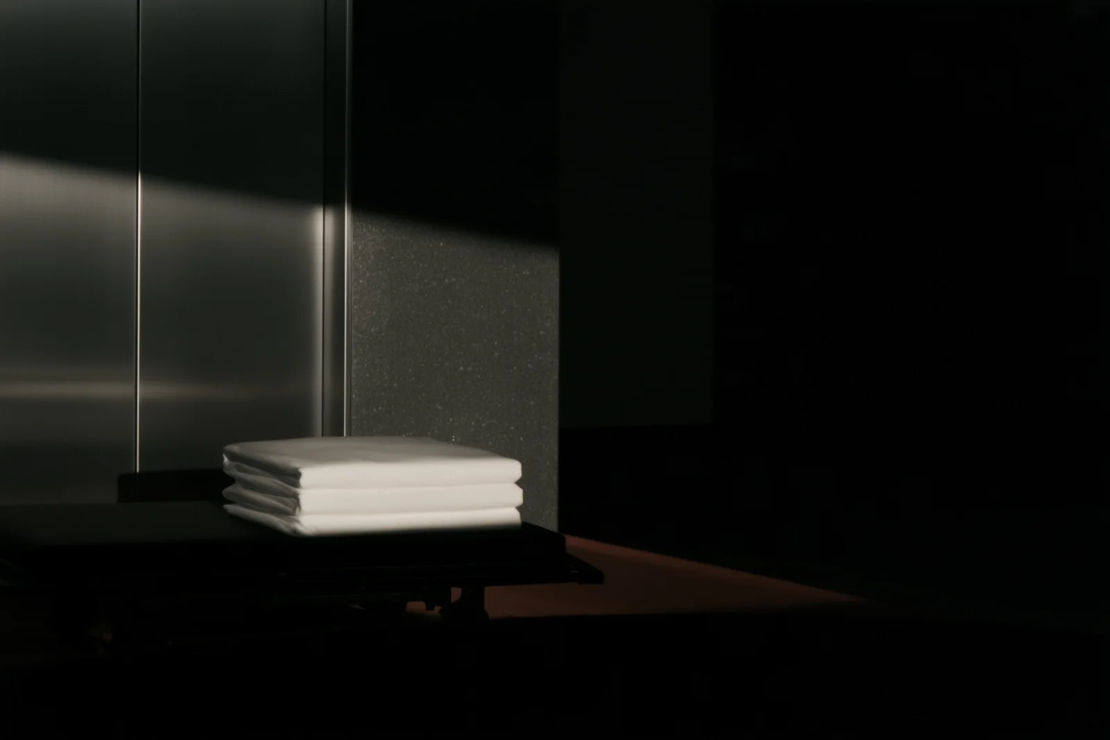 Folded linen beside metal surfaces and diagonal light.