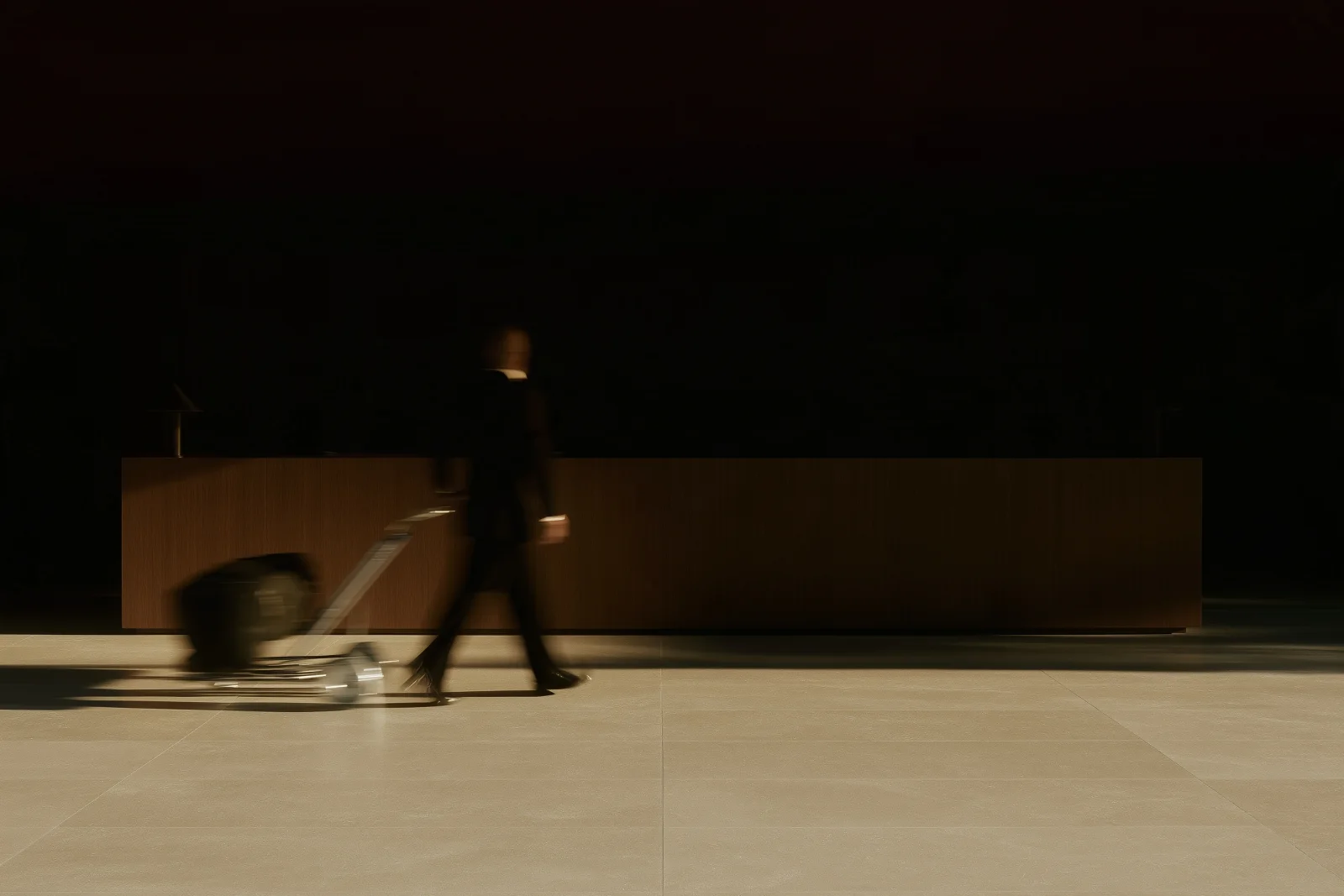 A figure seen from behind, moving with luggage past reception.