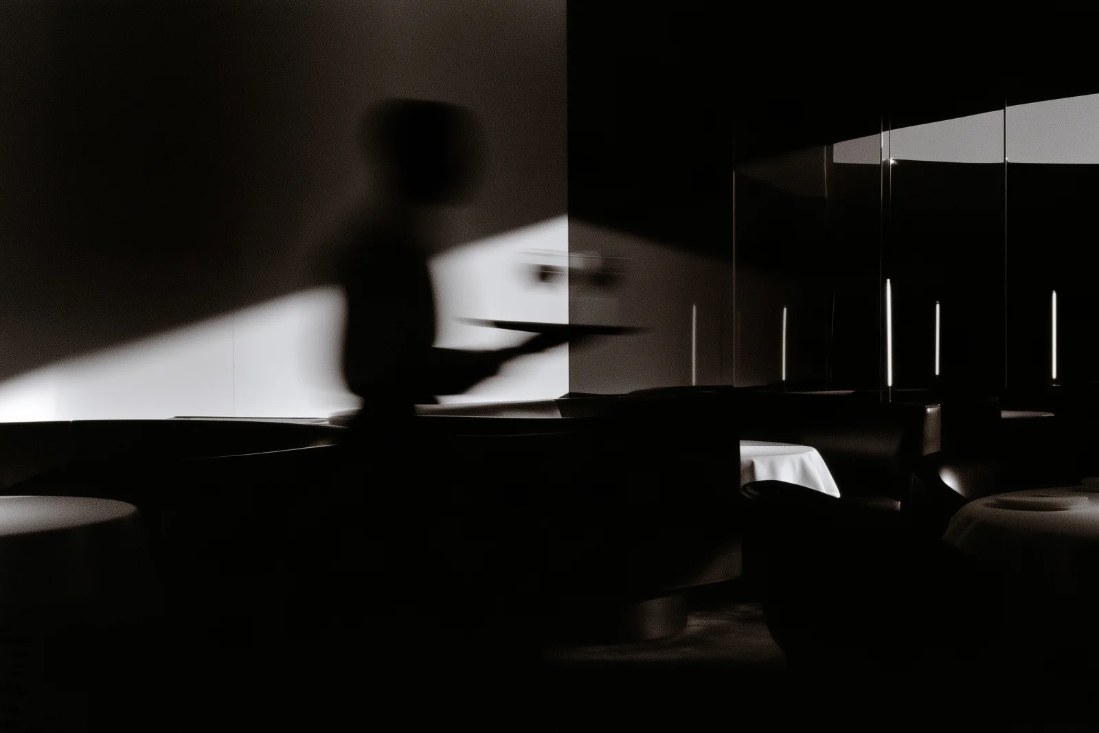 A blurred silhouette carrying a tray among restaurant tables and reflections.